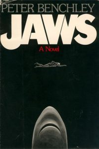 A book cover of Peter Benchley's Jaw in black background with a shark in the middle and woman swimming on top