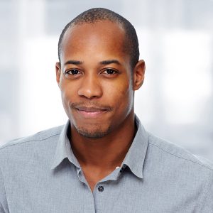A photo of a black man smiling and wearing grey collared polo in a white backgroun