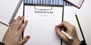 Hands of man holding a pen writing in a business plan paper