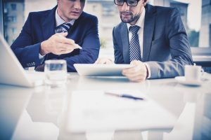 Image of two young businessmen discussing document in tablet at meeting