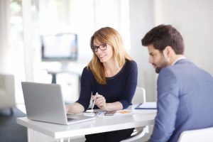 businesswoman sitting at office in front of computer and consulting with young professional man