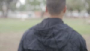A photo of a back of man wearing black jacket facing the field
